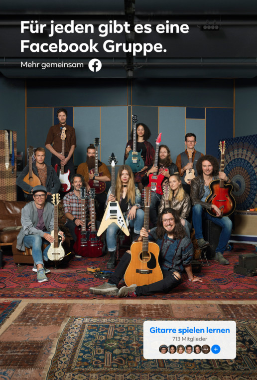 In einem Musikraum mit Sofas, Sessel und Hocker sitzen und stehen viele verschiedene Menschen mit ihren Gitarren.