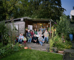 Inszeniertes Gruppenbild von Mitglieder von einem Familiengärtnerverein. Die Leute sitzen beisammen in einem Gartenhaus.