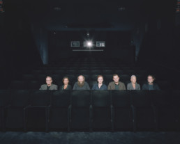 Inszeniertes Gruppenbild von Mitglieder von einem Filmclub. Diese sitzen alle in einer Reihe in einem Kinosaal.