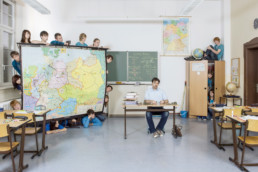 IN einem Klassenzimmer sitzt der Lehrer an seinem Lehrerpult und spielt mit Soldaten-Figuren. Alle Schüler und Schülerinnen verstecken sich: Hinter der Landkarte, auf und im Kasten,… .