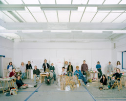 Inszeniertes Gruppenbild von Teilnehmer*innen einer Malklasse. Die Leute sitzen und sehen im grossen Zeichnungssaal hinter und neben Ihren Staffeleien.
