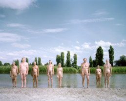 Inszeniertes Gruppenbild von Mitglieder der Interesse und Performancegruppe ‚Naked Projects‘. Die Männer und Frauen stehen alle nackt an einem Stadtsee