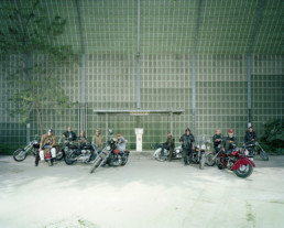Inszeniertes Gruppenbild von Motorradfahrer und Motorradfahrerinnen auf ihren Motorräder in einem Industriegebiet.