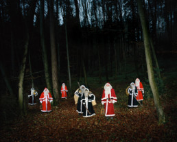 Inszeniertes Gruppenbild von mehreren Santikläusen und Schmutzlis in einem dunklen Wald. Sie stehen in ihrer Santiklause -Kleidung mit ihren vollgefüllten Säcken und Ruten zwischen den Bäumen.