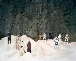 Inszeniertes Gruppenbild von Mitglieder einer Star-Wars- Gruppe. An einem futuristischen kargen Ort stehen die als Star-wars Figuren verkleideten Menschen. Im Hintergrund eine hohe dunkle Stein-Wand.